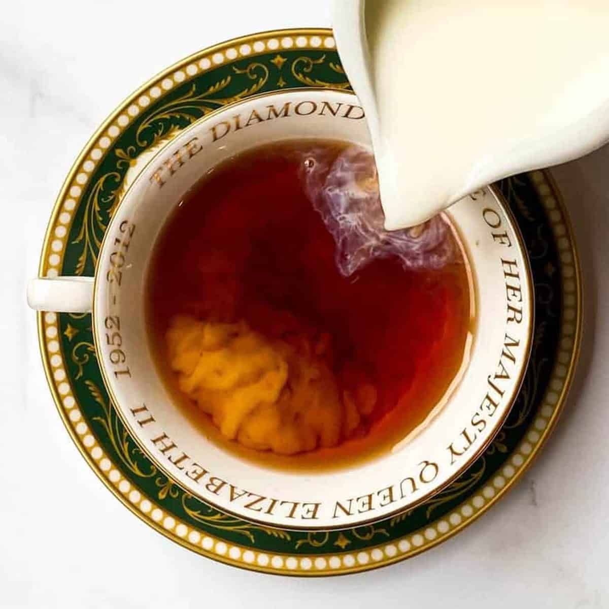 Cream being poured into Irish Breakfast Tea served in a Queen Elizabeth Jubilee teacup.