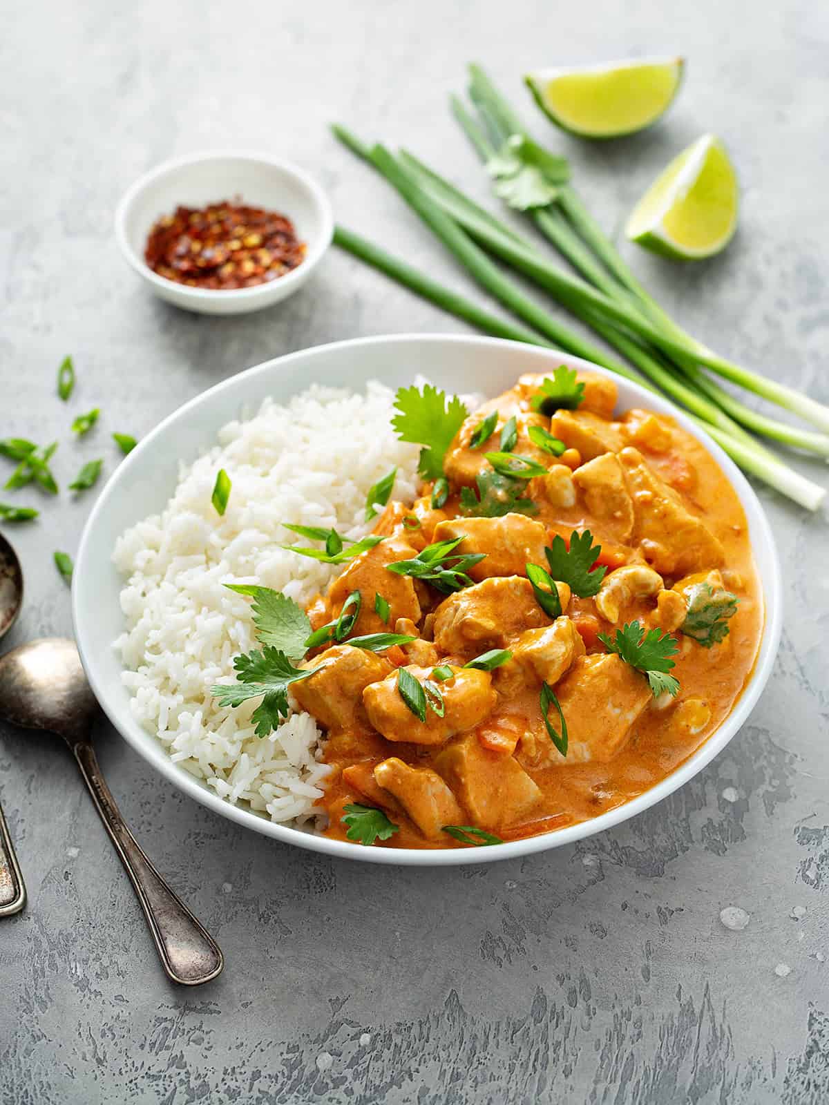 Bowl of quick cooking chicken curry over white rice with red pepper flakes on the side.