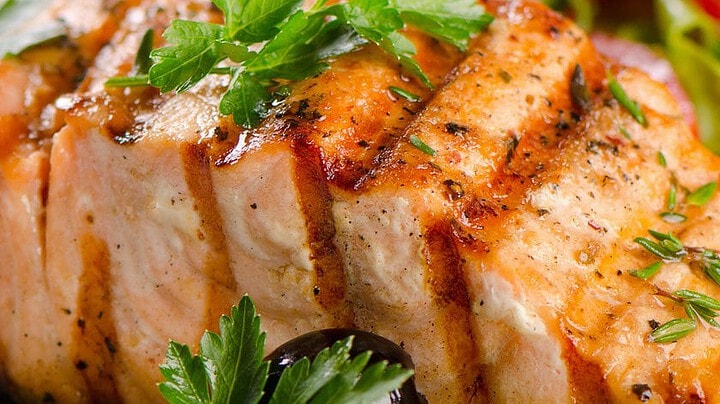 Enjoy a spring-inspired grilled salmon fillet, garnished with parsley, lemon slices, and black olives—served alongside fresh vegetables for one of your perfect April 20 minute dinners.