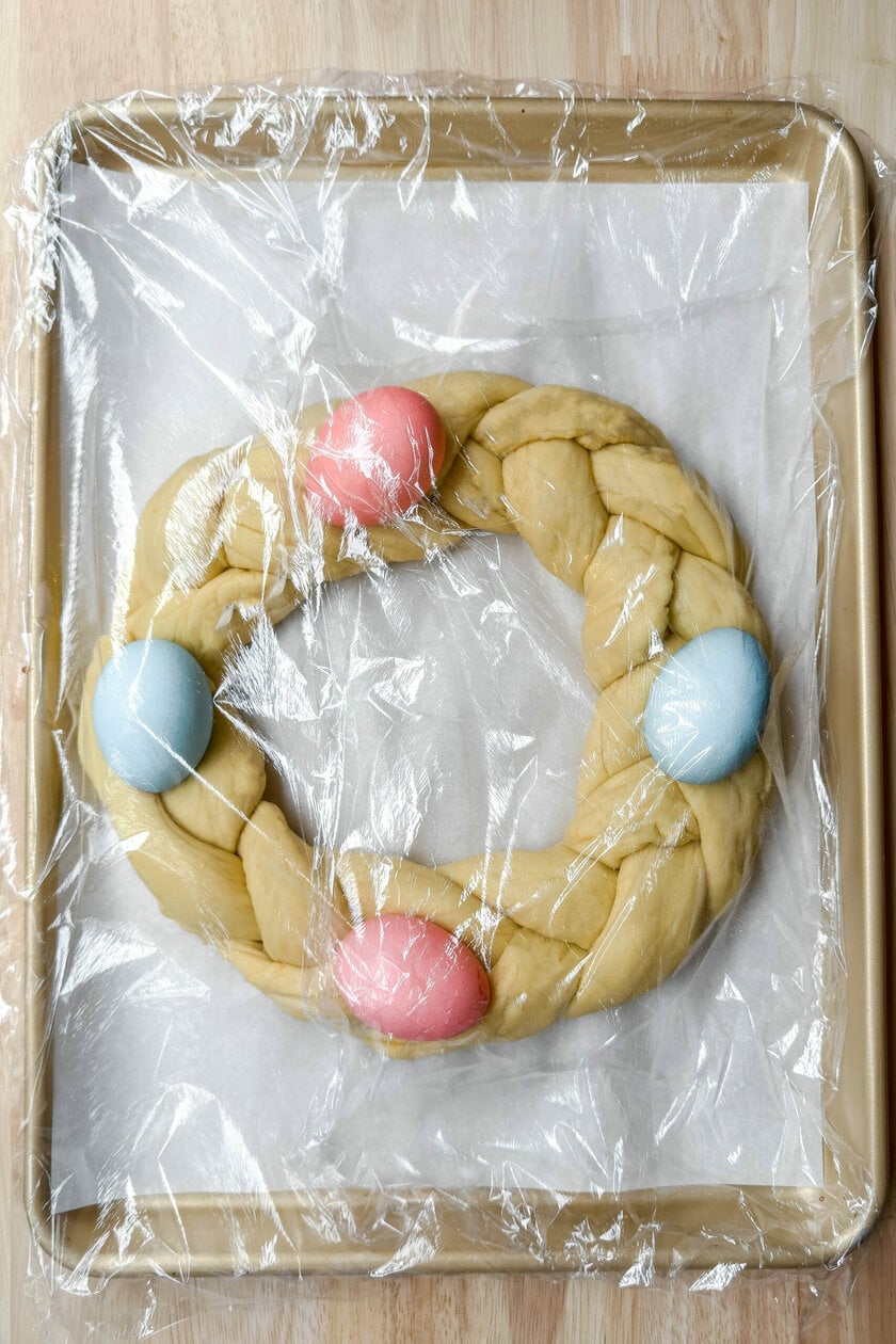 Top view of Easter bread, braided and shaped with dyed Easter eggs on top, covered and rising for the 2nd time.