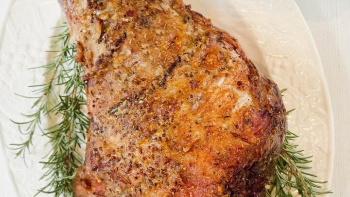 Top view of roasted Leg of Lamb on a white oval platter.