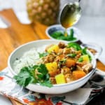 A bowl of coconut rice and pineapple pork with colorful bell peppers and pineapple is garnished with cilantro, while a savory Pineapple Pork sauce is being drizzled from a spoon above.