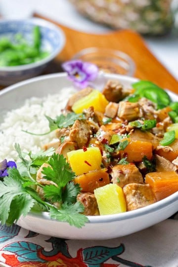 A bowl of coconut rice and pineapple pork in teriyaki sauce garnished with cilantro in a bowl.