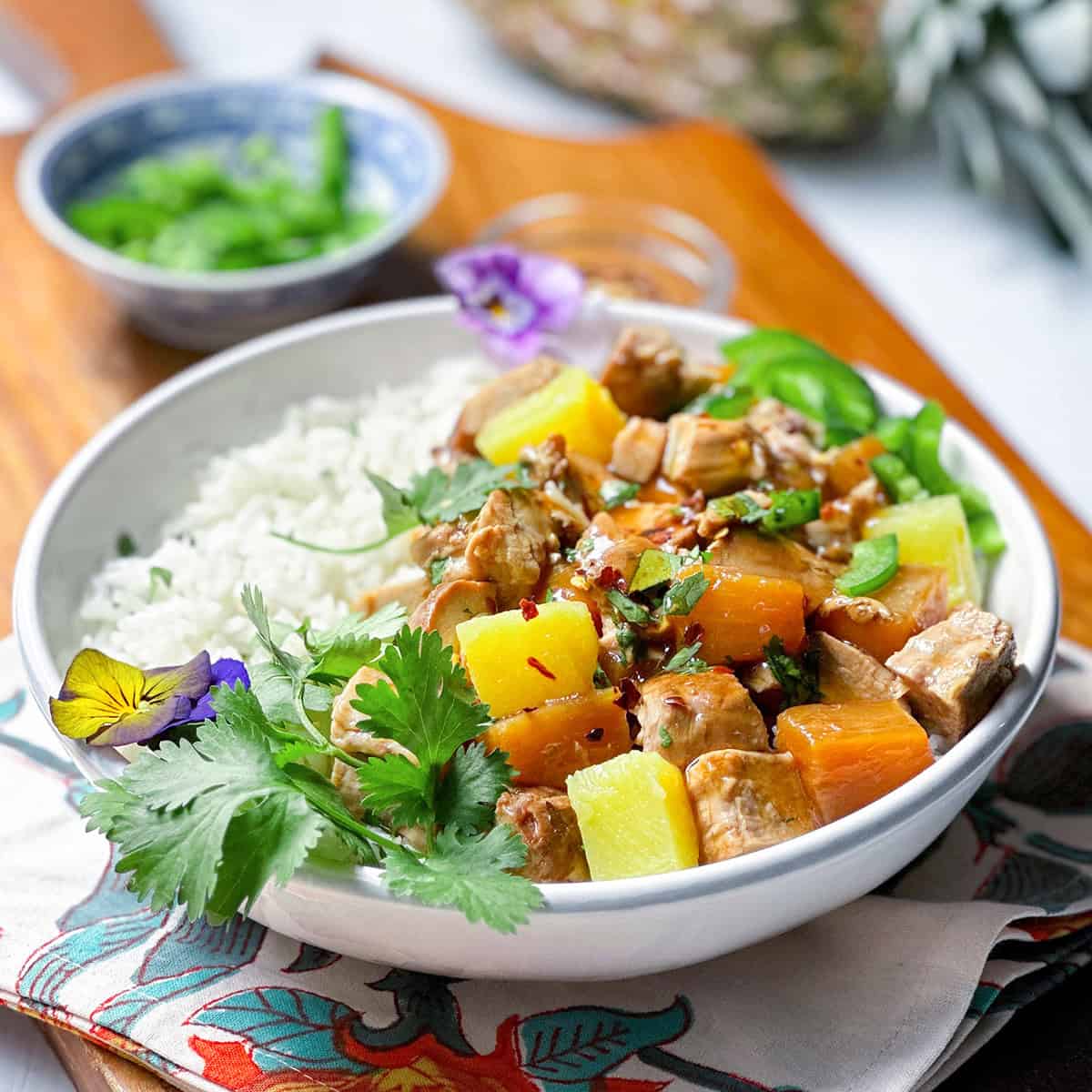 A bowl of coconut rice and pineapple pork in teriyaki sauce garnished with cilantro in a bowl.