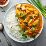 Bowl of steamed rice and quick chicken curry in a whole with fresh cilantro and green onion garnishes.