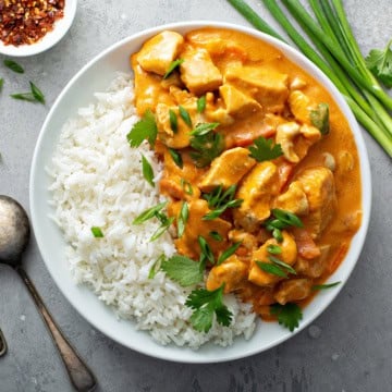 Bowl of steamed rice and quick chicken curry in a whole with fresh cilantro and green onion garnishes.
