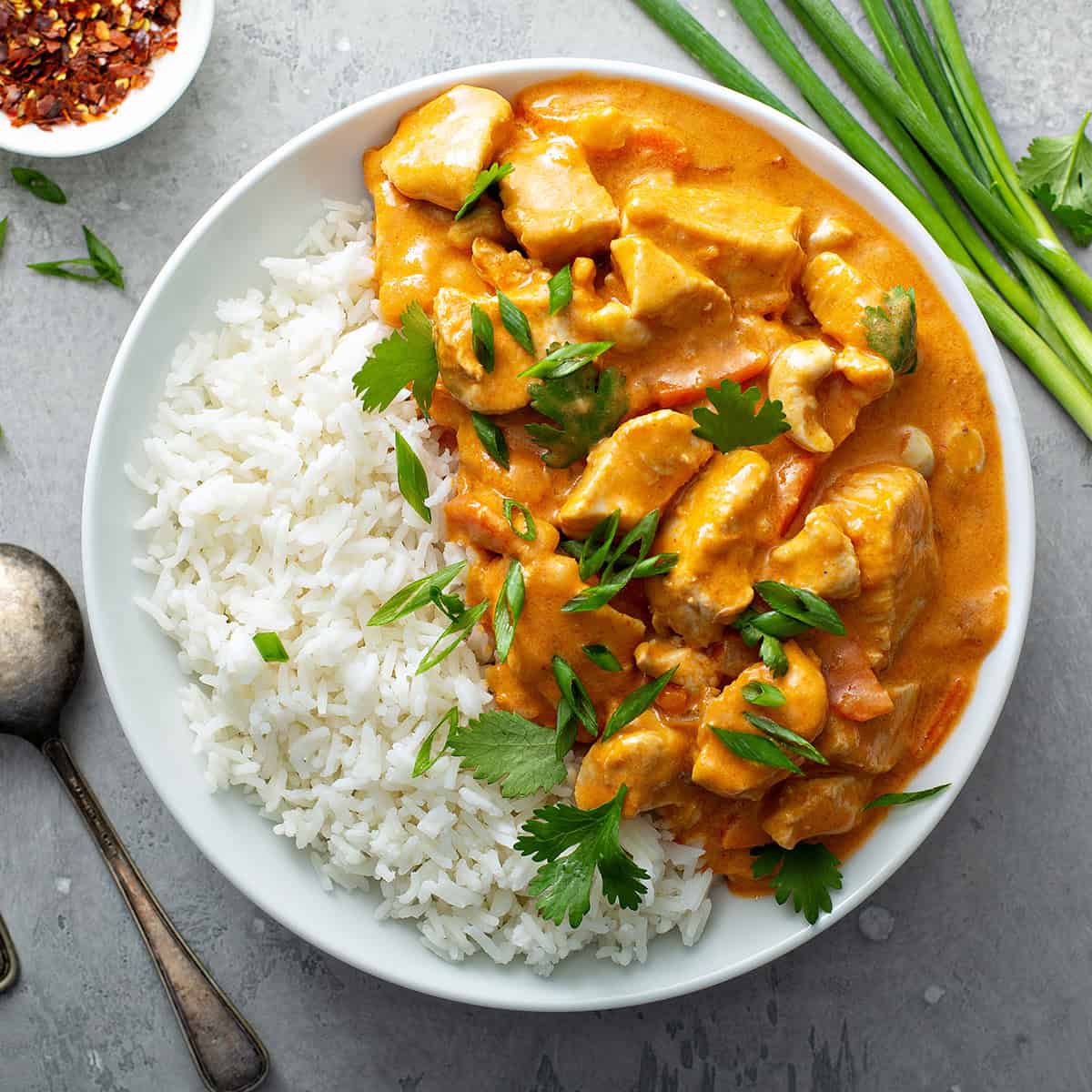 Bowl of steamed rice and quick chicken curry in a whole with fresh cilantro and green onion garnishes.