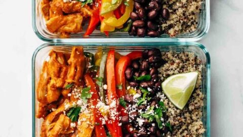 Three glass meal prep containers filled with shredded chicken, sliced bell peppers, black beans, quinoa, and lime wedges—these Healthy Sheet Pan Dinners are arranged neatly in rows for convenient and nutritious meals.