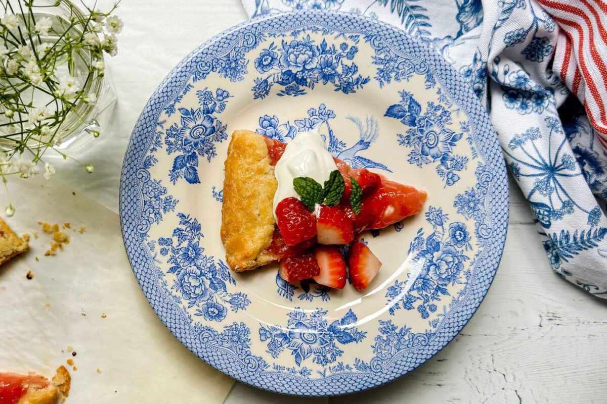 Top view of Strawberry Rhubarb Crostata slice with fresh mint, strawberries and whipped cream on a blue and white plate