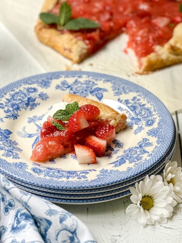 Side view of sliced Strawberry Rhubarb Tart on a blue and white plate with fresh mint leaves