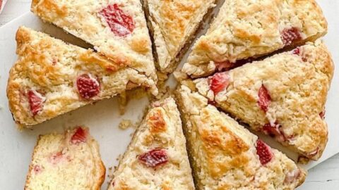 Top view of sliced Strawberry Scone Loaf on a white marble board with clotted cream and butter