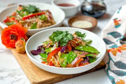 Side view of Curried Singapore Noodles with fresh cilantro in a white bowl with sesame seeds