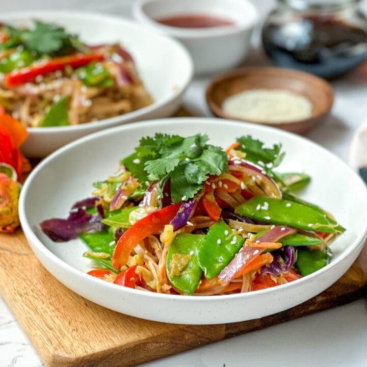 Side view of Curried Singapore Noodles with fresh cilantro in a white bowl with sesame seeds
