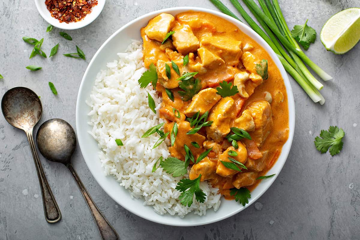 Top view of Chicken Curry in a white bowl with rice and fresh herbs.
