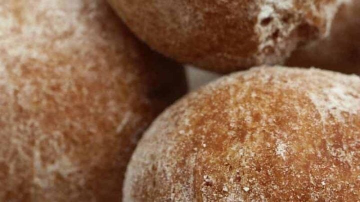 Three round, golden-brown doughnuts dusted with powdered sugar are stacked on a white lace doily—perfect for savoring after enjoying one of your favorite May One Pot Dinners.