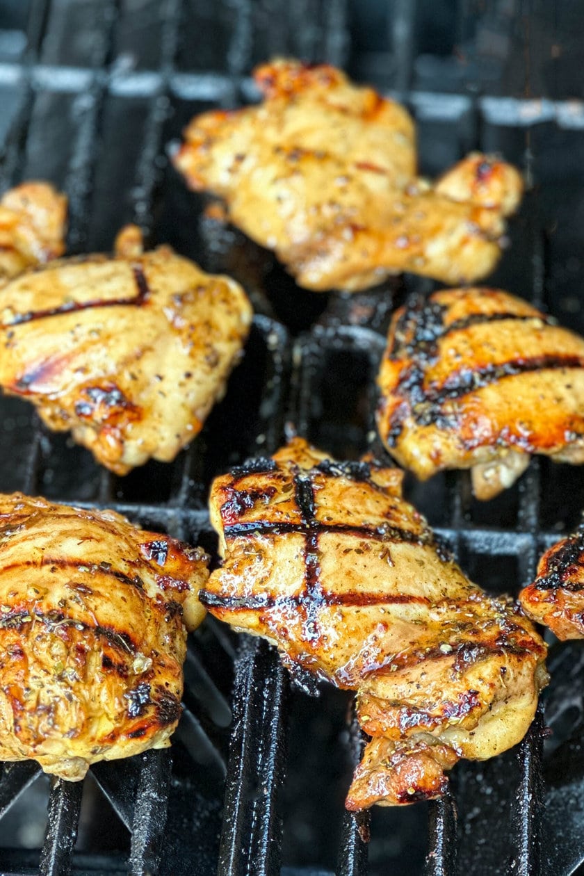 Side view of chicken thighs grilling on a BBQ grate.