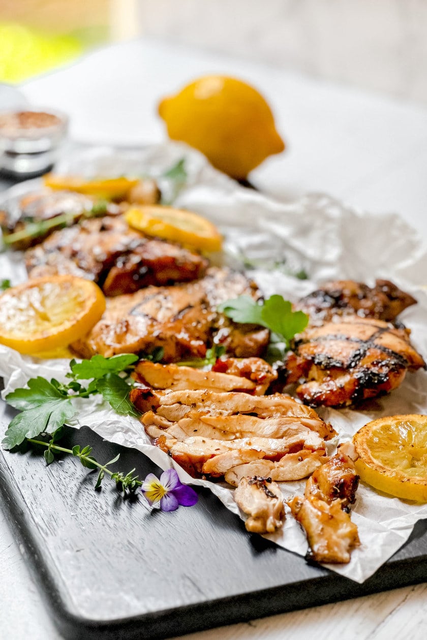 Side view of grilled chicken thighs with sliced meat, fresh herbs on a parchment lined cutting board