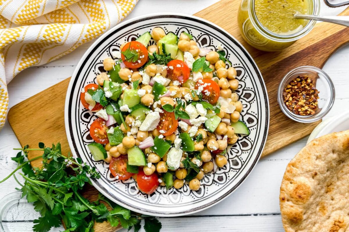 Horizontal top view of Chickpea Salad on a black and white plate with fresh herbs, cucumbers and feta cheese