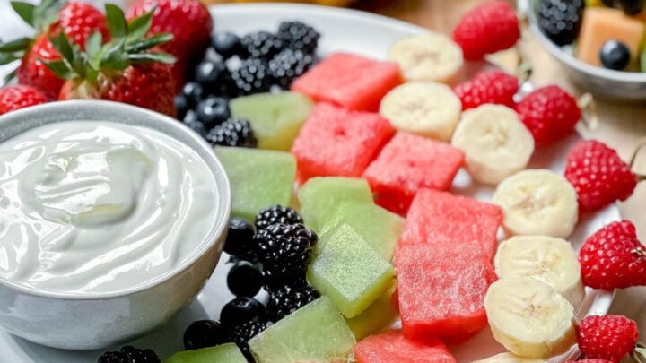 Closeup side view of fruit skewers and yogurt dip on a white plate