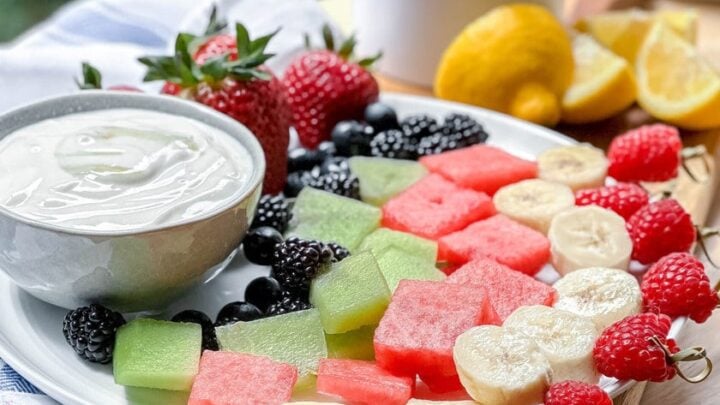 Side view of Fruit Skewers and Yogurt Dip on a white platter with fresh lemons and strawberries