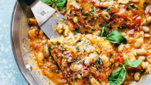 A stainless steel pan containing cooked chicken breasts in a creamy tomato and white bean sauce, garnished with fresh basil leaves—a perfect choice for healthy skillet dinners for May.