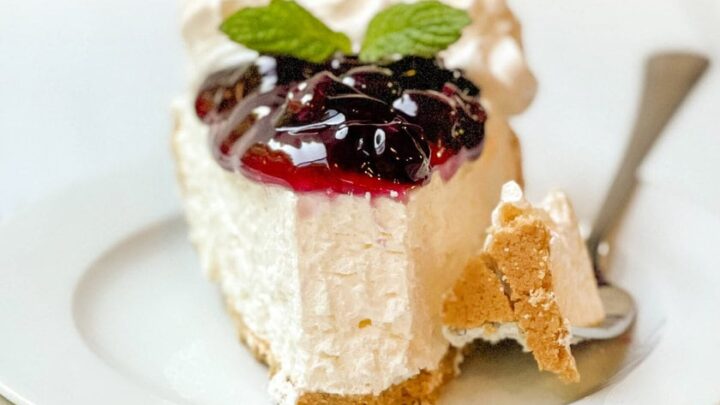 Front side view of 10 minute easy no-bake cheesecake topped with blueberry sauce, and fresh mint, with a bite missing on a white plate.