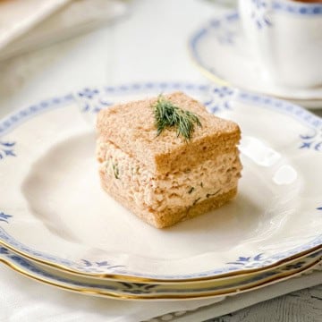 Salmon salad tea sandwich with creamy salmon and dill filling on whole wheat bread, garnished with fresh dill.