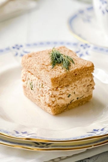 Salmon salad tea sandwich with creamy salmon and dill filling on whole wheat bread, garnished with fresh dill.