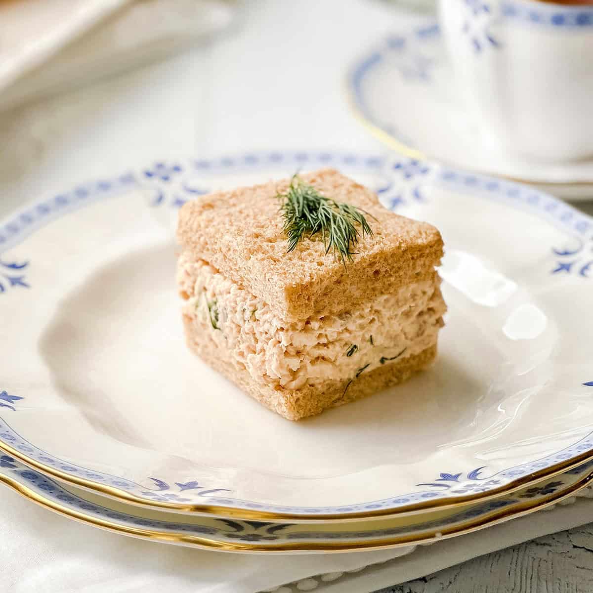 Salmon salad tea sandwich with creamy salmon and dill filling on whole wheat bread, garnished with fresh dill.