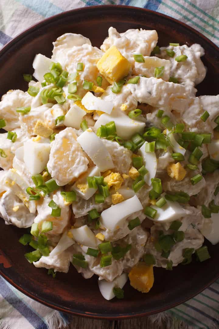 A plate of potato salad recipe with chopped hard-boiled eggs, green onions, and mayonnaise served on a checkered cloth.