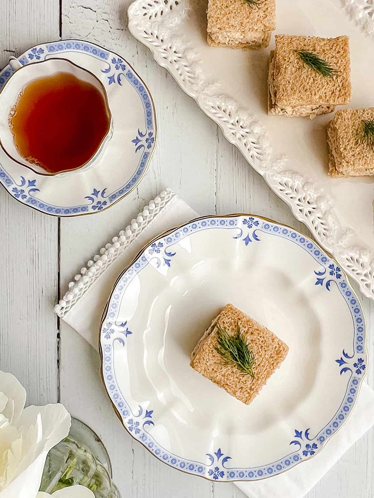 Overhead view of salmon salad tea sandwiches garnished with dill and served on a white tray with tea.