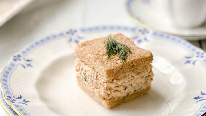 Side view of single Salmon Salad Tea Sandwich on a white and white plate with tea