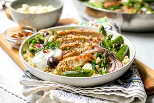 Side view of Greek Chicken Skillet in a white bowl over Israeli Couscous