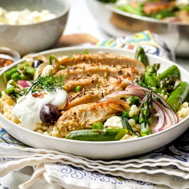 Side view of Greek Chicken Skillet in a white bowl over Israeli Couscous