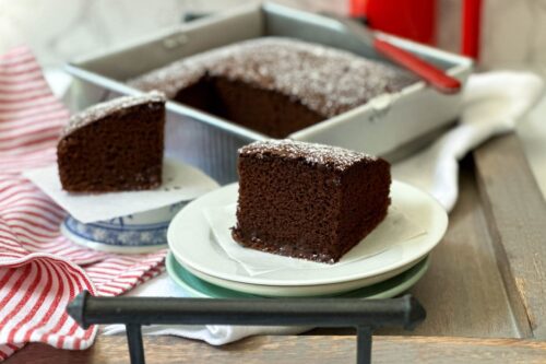 Side view of a slice of Picnic Chocolate Cake on a white plate with more in the background