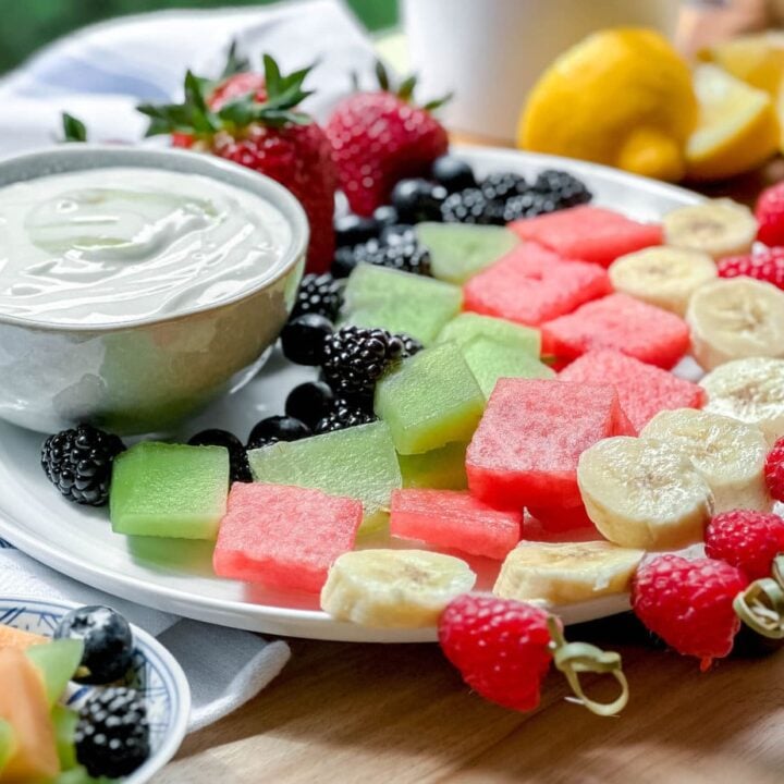 Side view of fruit skewers on a plate with yogurt dip and fresh strawberries