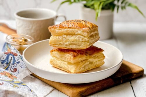 Side view of two baked Ham and Cheese Croissants on a white plate with coffee