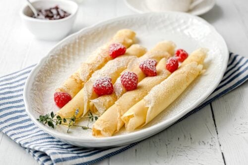 Side view of Swedish Pancakes with fresh raspberries on an oval white platter
