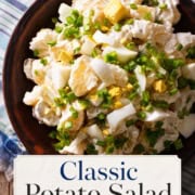 A bowl of classic potato salad with chopped hard-boiled eggs and green onions, set on a blue plaid cloth with a "Potato Salad Recipe" label.