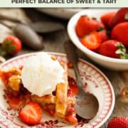 A slice of strawberry rhubarb pie topped with vanilla ice cream sits on a plate, surrounded by fresh strawberries and a spoon ready for the perfect bite.