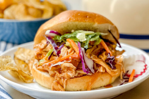 Side view of BBQ Chicken on a bun with coleslaw and potato chips