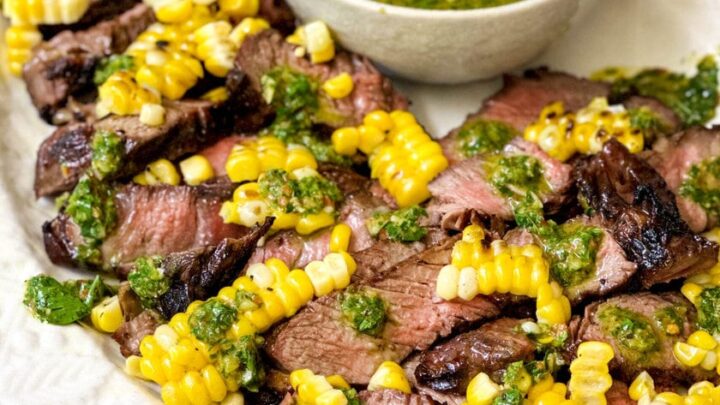 Side view of sliced ribeye steak, corn kernels, and chimichurri sauce drizzled over the top