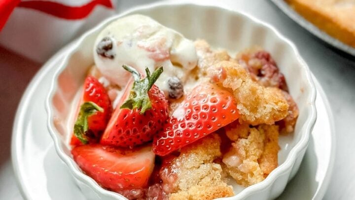 Top side view of a serving of strawberry cobbler in a white tart dish with melting vanilla ice cream