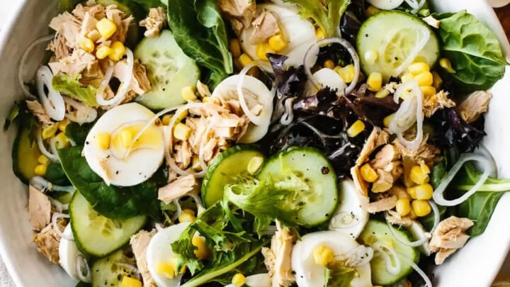 Top closeup view of tuna cucumber salad with fresh herbs, greens, cucumbers, and corn.