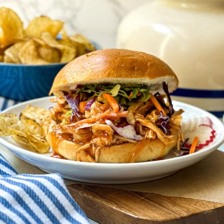 Side view of 3 ingredient Slow Cooker BBQ Chicken on a bun with coleslaw and chips
