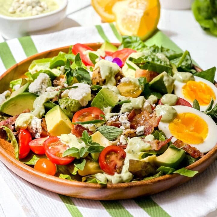 Closeup side view of Chicken Cobb Salad with lemon wedges, tomatoes, hard boiled eggs and avocado chunks in a wooden salad bowl