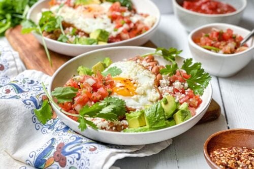 Closeup side view of Huevos Rancheros in a white breakfast bowl with fried eggs, salsa and pinto beans on a corn tortilla
