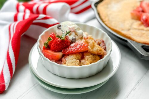 Top side view of Skillet Strawberry Cobbler in a white ramekin with melting swiss almond vanilla ice cream