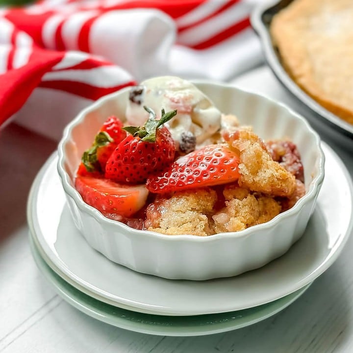 Top side view of Skillet Strawberry Cobbler in a white ramekin with melting swiss almond vanilla ice cream
