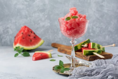 Side view of watermelon granita with wedge shaped watermelon in the background